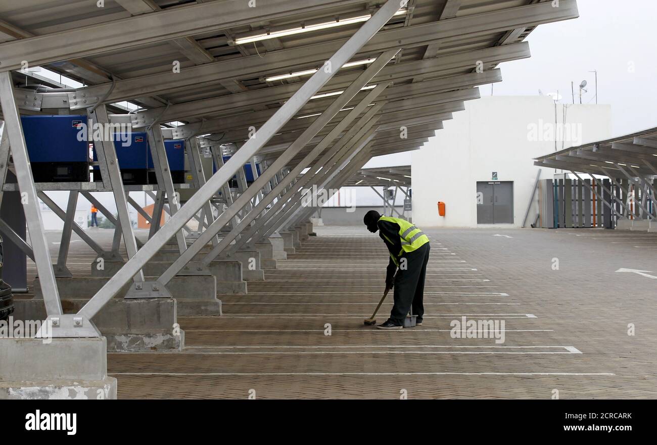 A worker sweeps the floor under solar panels which provide shade for vehicles at a solar carport at the Garden City shopping mall in Kenya's capital Nairobi, September 15, 2015. The Africa's largest solar carport with 3,300 solar panels will generate 1256 MWh annually and cut carbon emission by around 745 tonnes per year, according to Solarcentury and Solar Africa.  REUTERS/Thomas Mukoya Stock Photo