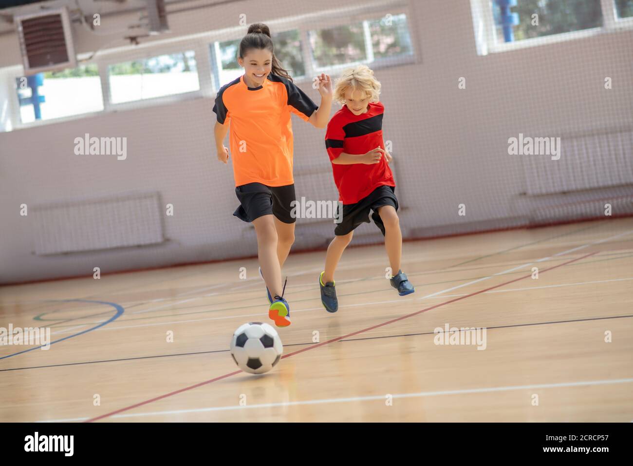 Three kids in sportswear running after the ball in the gym Stock Photo