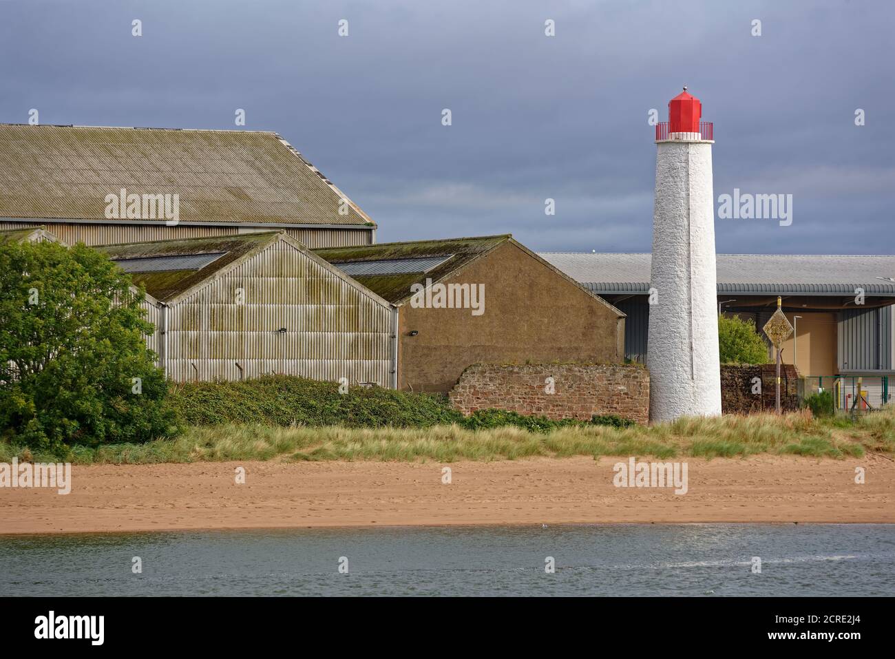 The Old Montrose Rear Lighthouse next to the Beach and beside some Old Warehouses with Galvanised Sides and Roofs, and an Old stone wall. Stock Photo