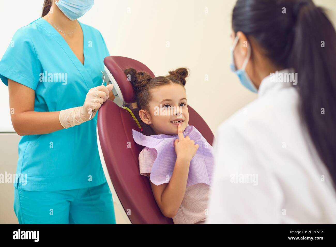 Smiling girl sitting in dental chair and showing front teeth to dentist Stock Photo