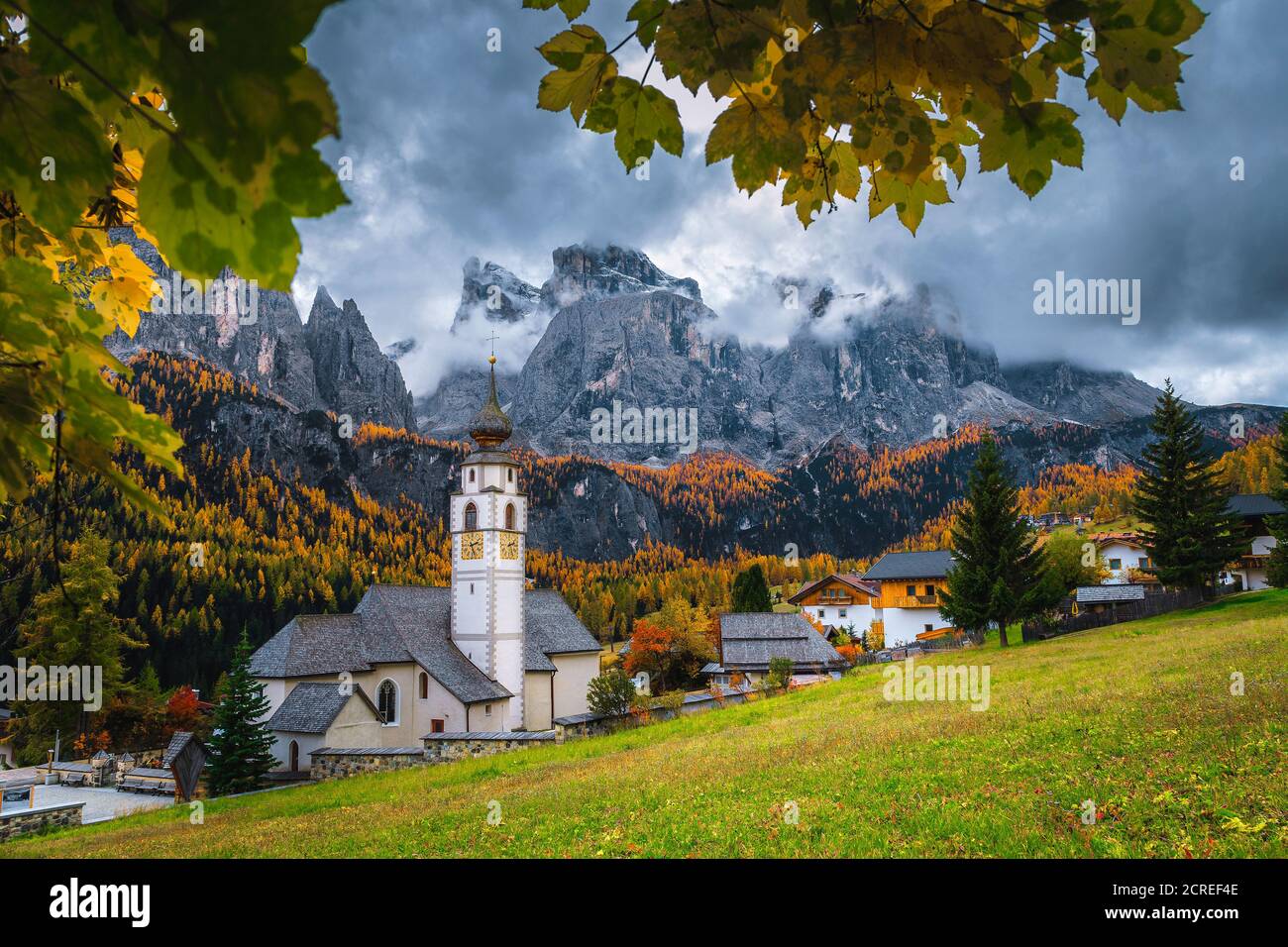 Amazing autumn scenery with colorful larch forest. Charming alpine village with beautiful church. Great hiking and touristic places, Colfosco, Dolomit Stock Photo