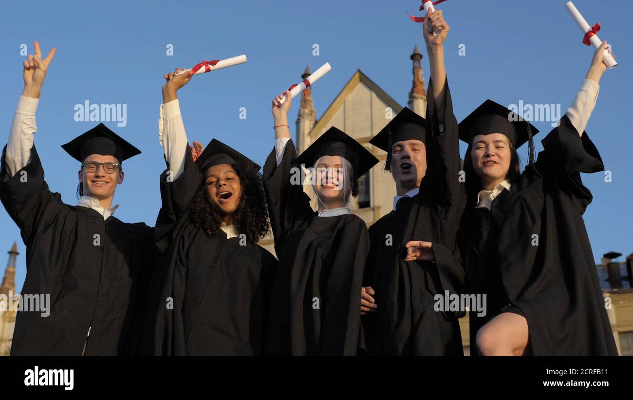 Happy group of students with arms up at their graduation. Stock Photo
