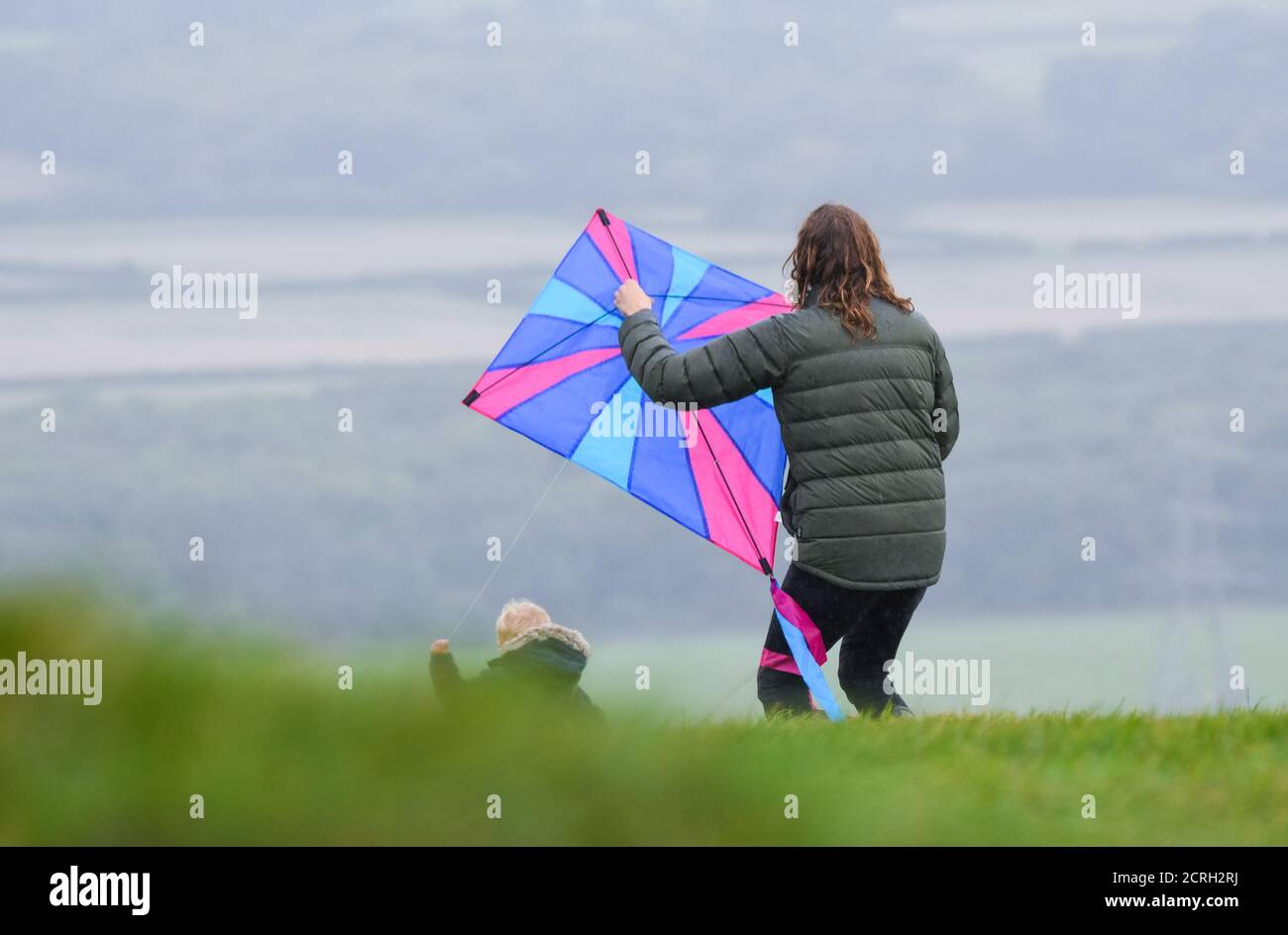 Woman and child flying a large kite from a hill in poor, wet & windy weather in the UK. Stock Photo