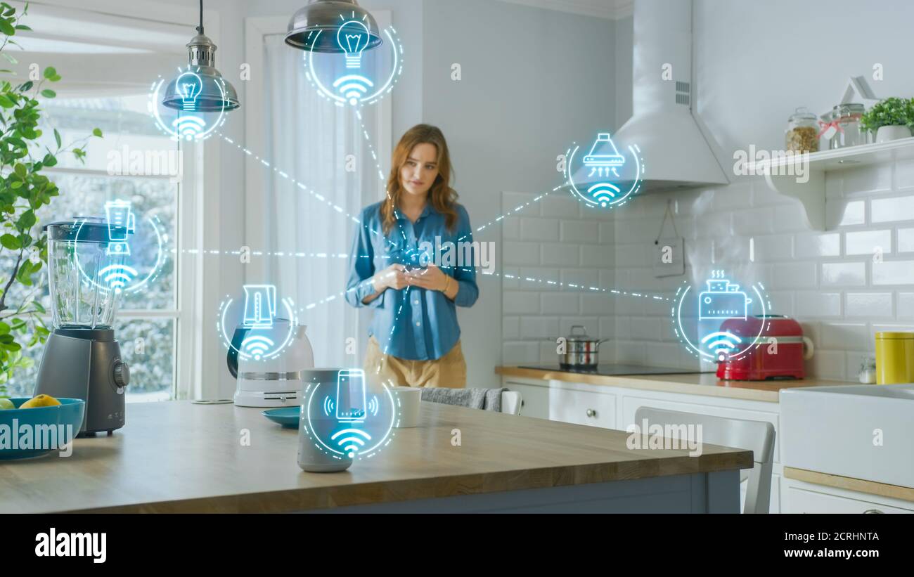 Internet of Things Concept: Young Woman Using Smartphone in Kitchen. She controls her Kitchen Appliances with IOT. Graphics Showing Digitalization Vis Stock Photo