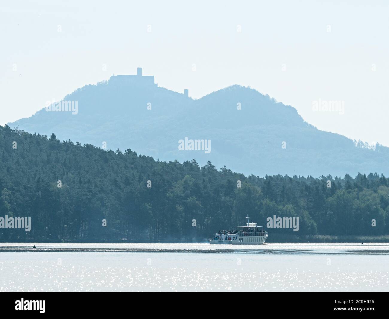 Tourist cruise boat on Machovo lake at Doksy town. The silhouette of Bezdez hill with Bezdez castle on the peak in background. Stock Photo