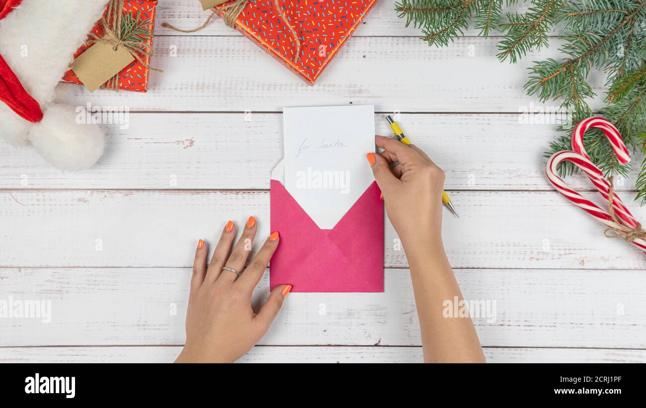 The young girl written letter to Santa Claus and puts them in an envelope, flat lay. Christmas decorations and gift box on wooden desk, top view. Conc Stock Photo