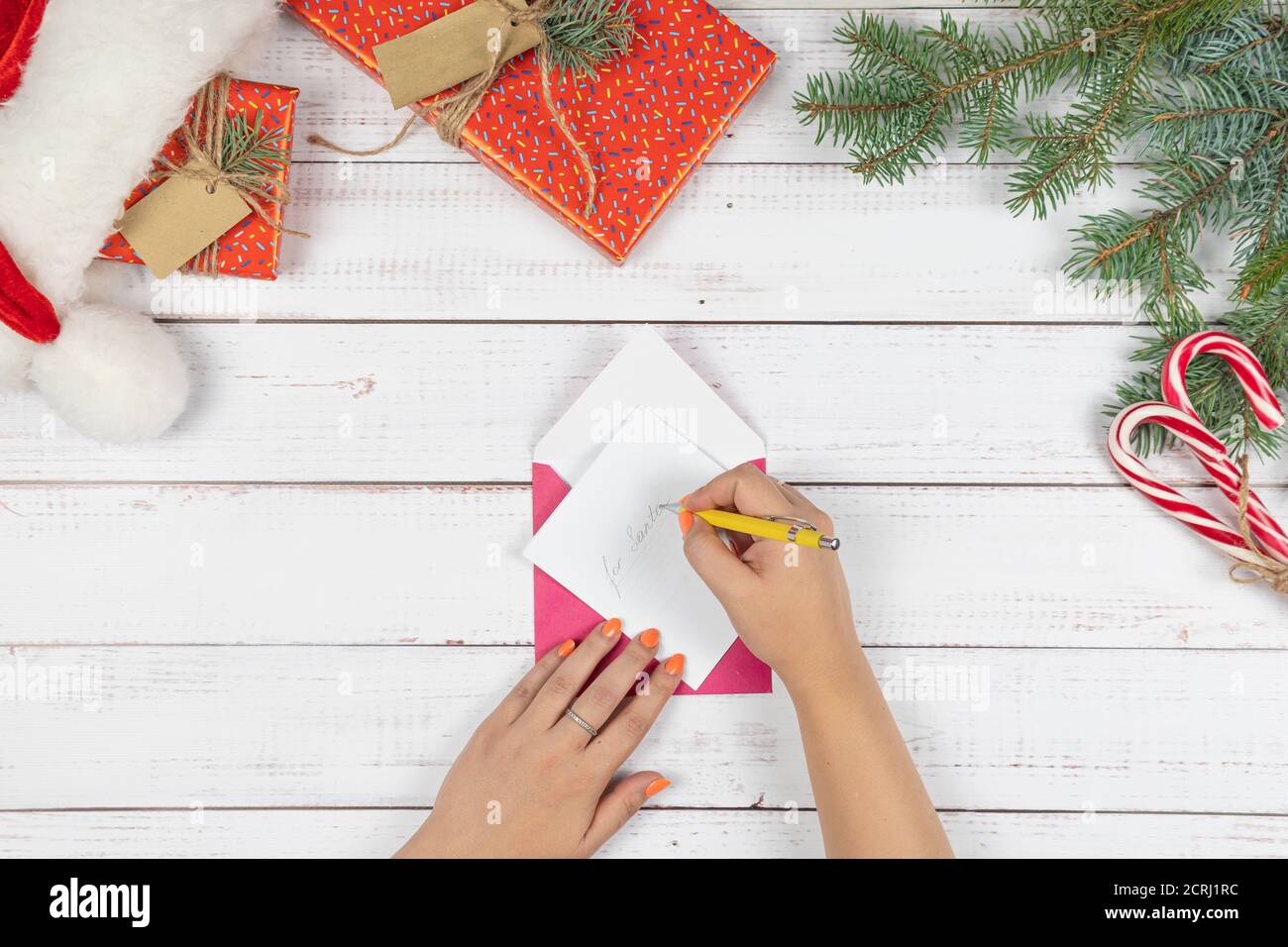 The young girl written letter to Santa Claus and puts them in an envelope, flat lay. Christmas decorations and gift box on wooden desk, top view. Conc Stock Photo