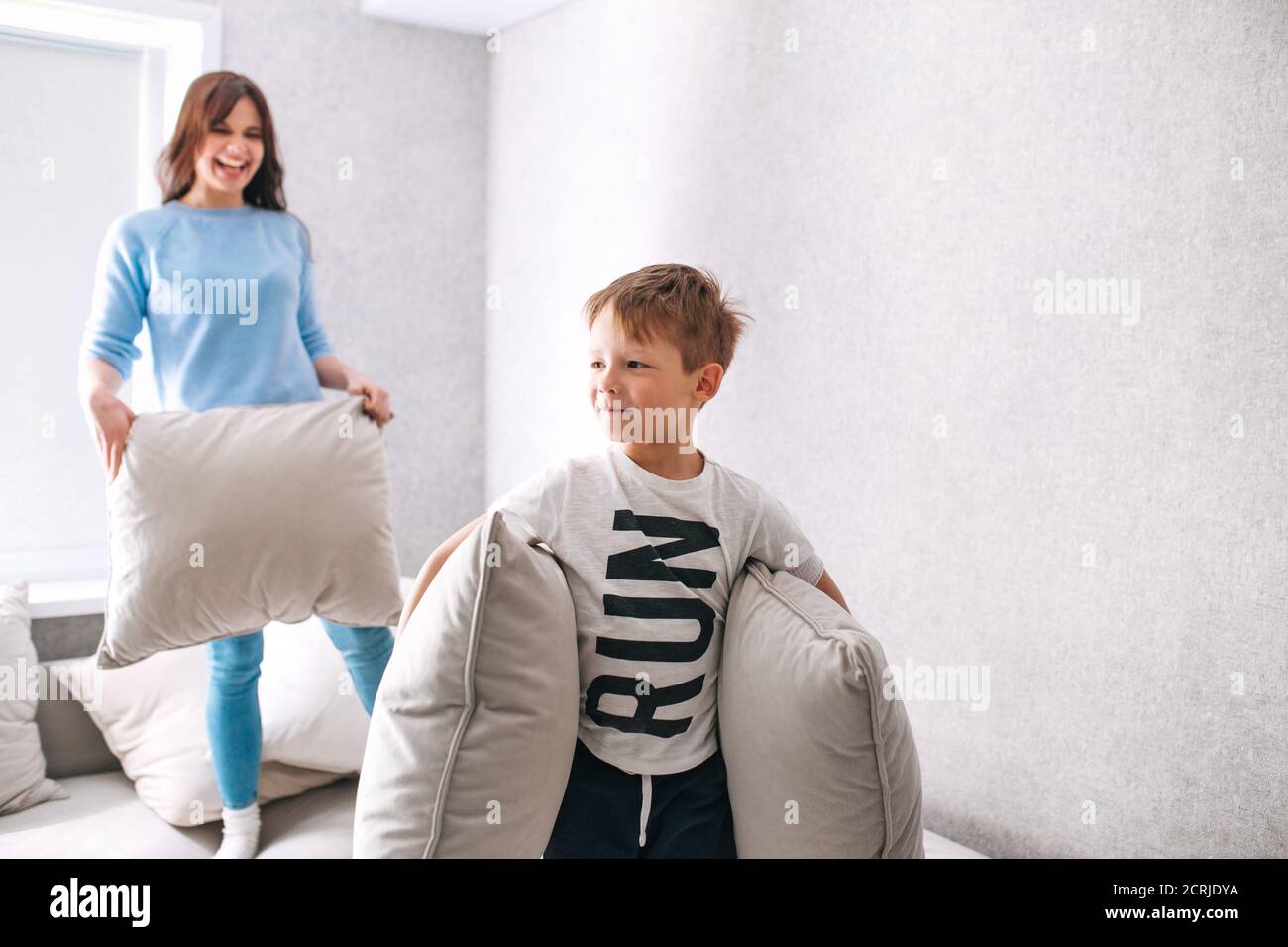 Son and mother having a pillow fight on sunny morning at home Stock Photo