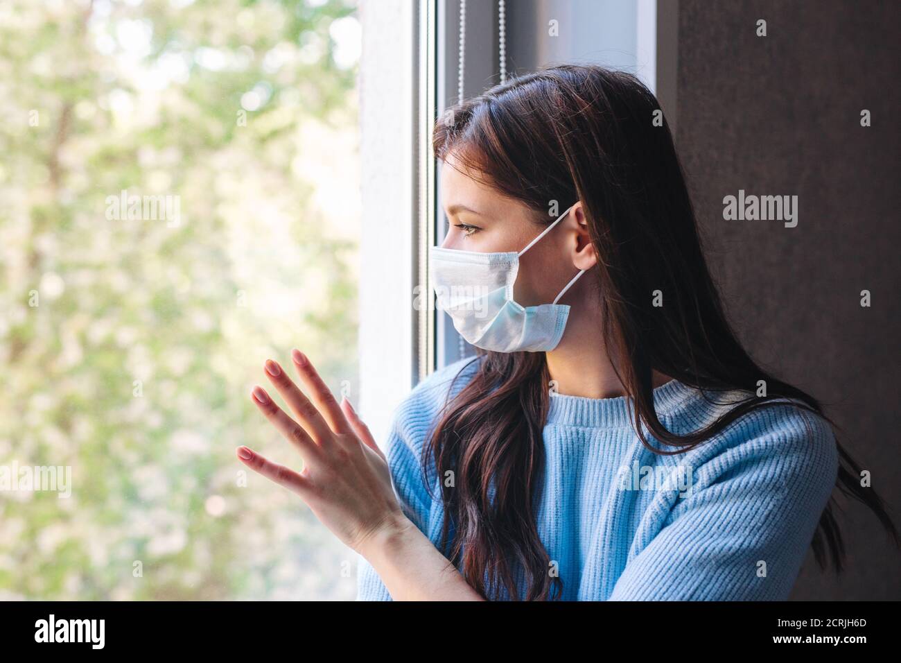 Young woman in quarantine wearing a protective mask and looking through