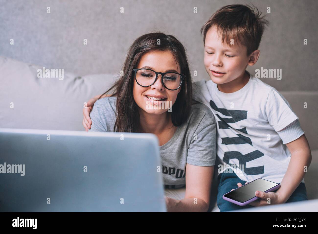 Little boy and his mother in video conference with teacher on laptop at home. Stock Photo