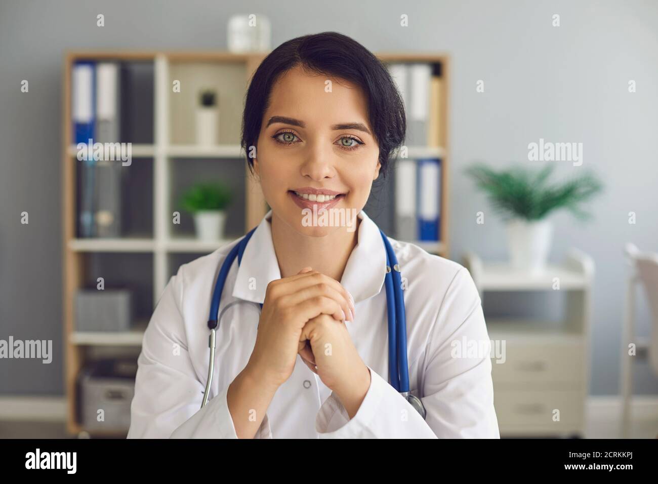 Friendly young doctor looking at camera during online consultation in her modern hospital office