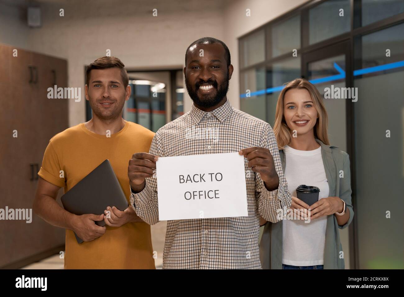 Covid 19 and business, young cheerful african office worker showing paper with text BACK TO OFFICE at camera and smiling while standing with his Stock Photo