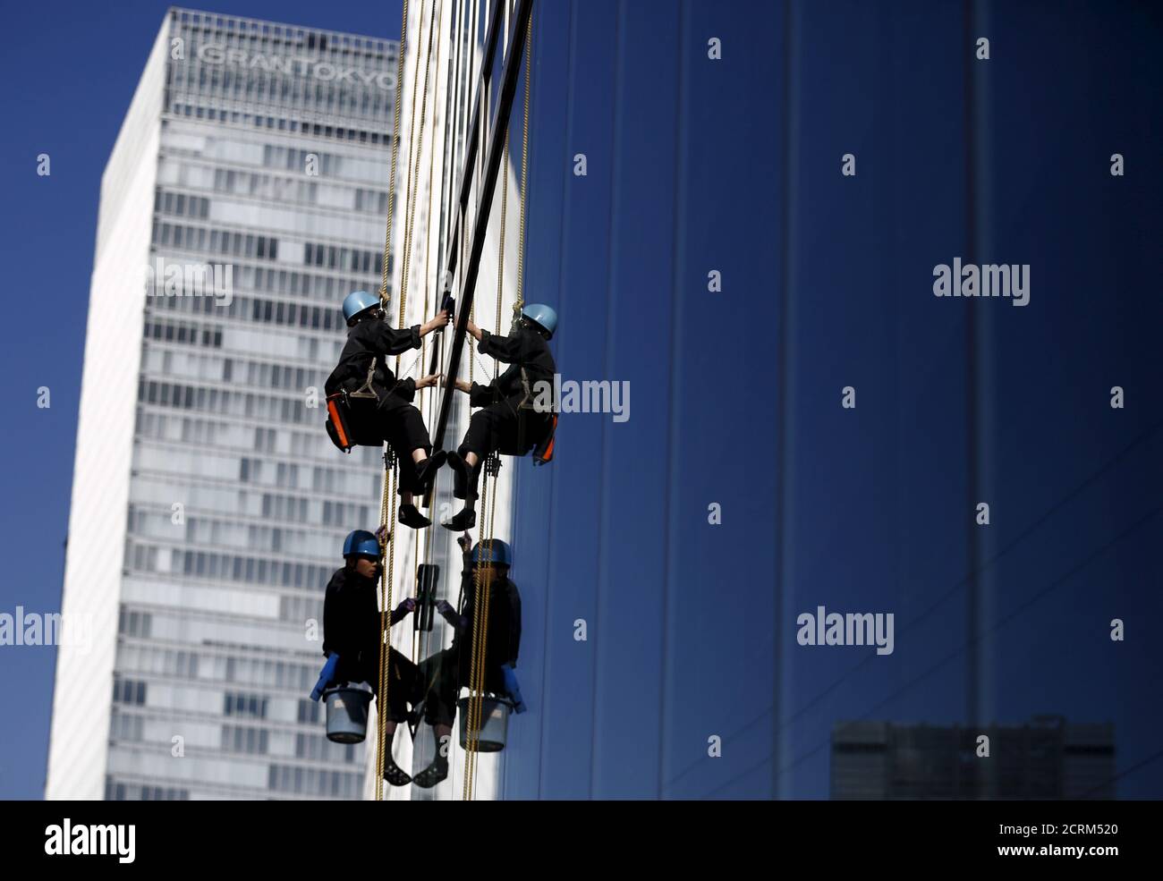 Workers clean windows at an office building in a business district in Tokyo, Japan, February 16, 2016. The Bank of Japan's negative interest rates came into effect on Tuesday in a radical plan already deemed a failure by financial markets, highlighting Tokyo's lack of options to spur growth as global markets sputter.  REUTERS/Thomas Peter Stock Photo