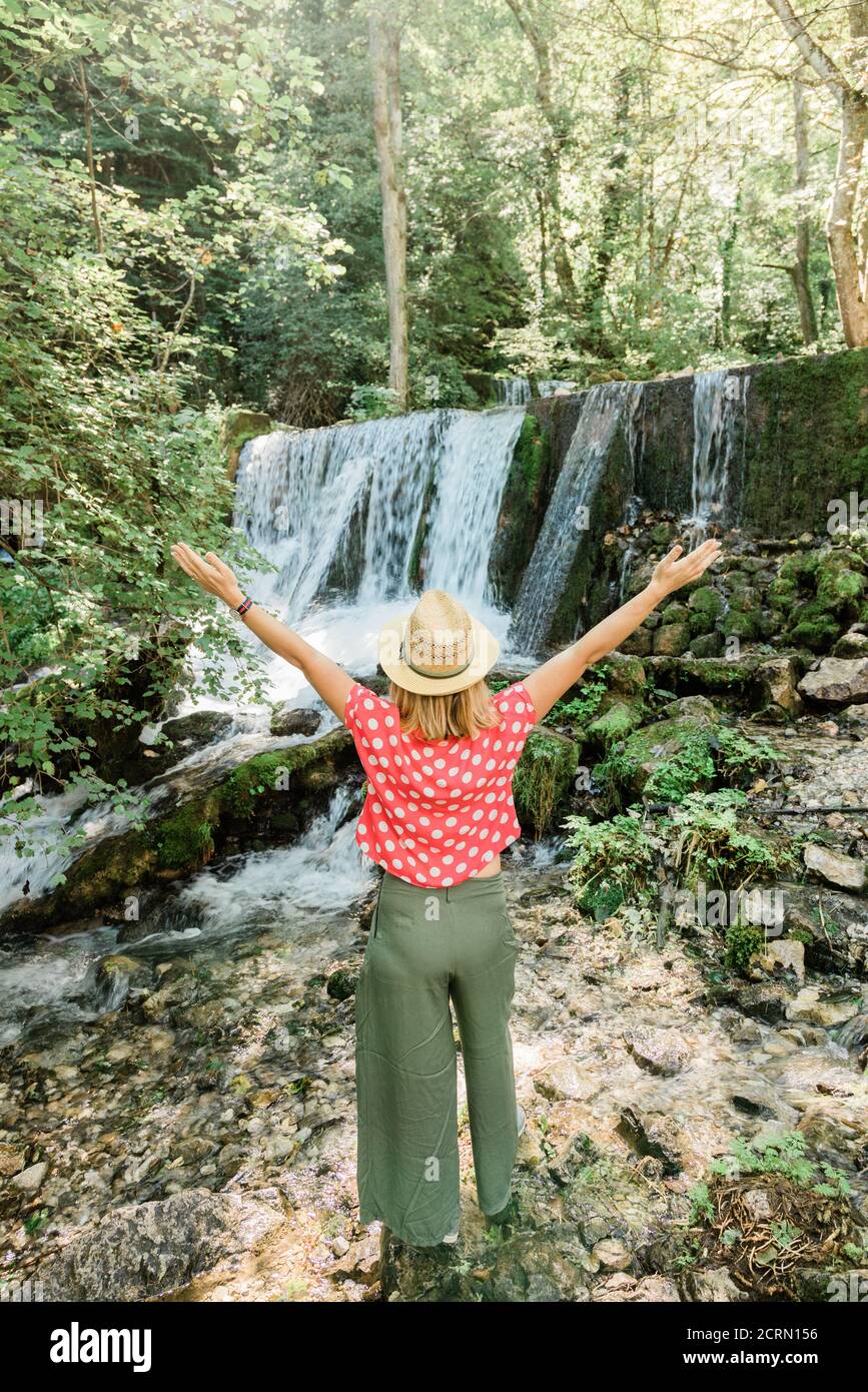 Young female nature explorer standing in front of the waterfall Stock Photo
