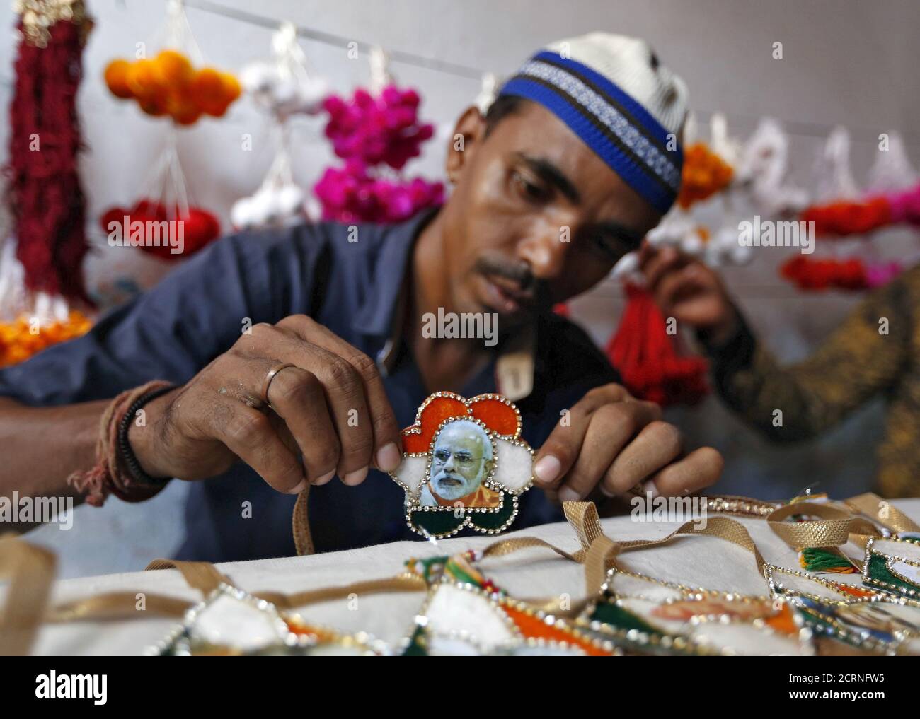 A Muslim artisan displays a 'rakhi' or traditional Indian sacred thread, featuring India's Prime Minister Narendra Modi after giving it the finishing touches inside a workshop in Ahmedabad August 17, 2015. Rakhi is also the name of a Hindu festival, also known as Raksha Bandhan, during which a sister ties one or more of the sacred threads onto her brother's wrist to ask him for her protection. The festival will be celebrated across the country on August 29 this year. REUTERS/Amit Dave Stock Photo
