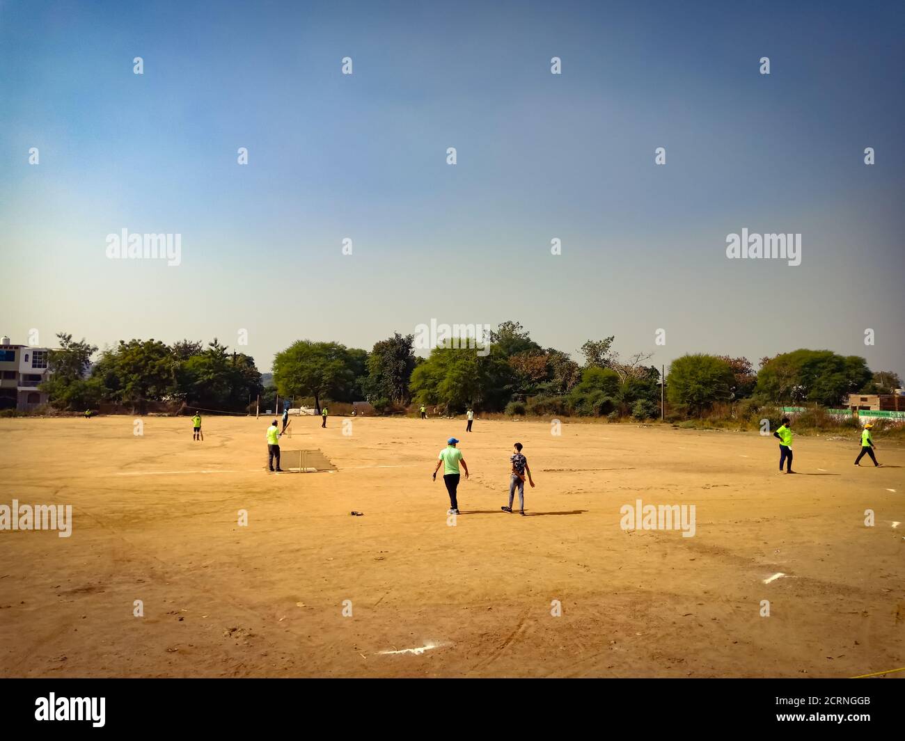 Indian people playing cricket on soil field at blue sky background. Stock Photo