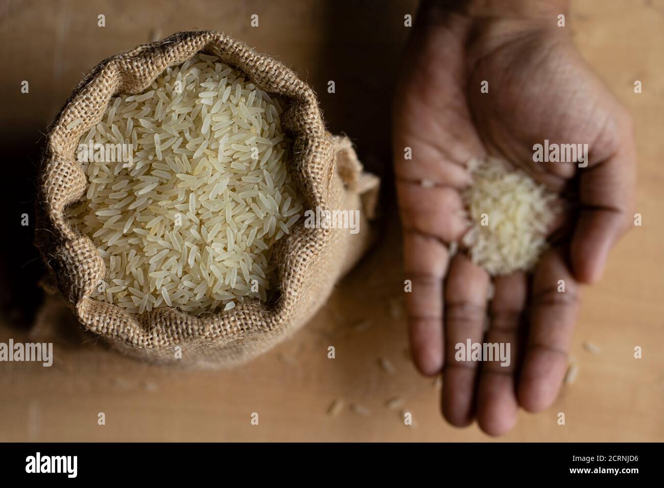 jute bag of rice and human hand with rice above wooden floor background