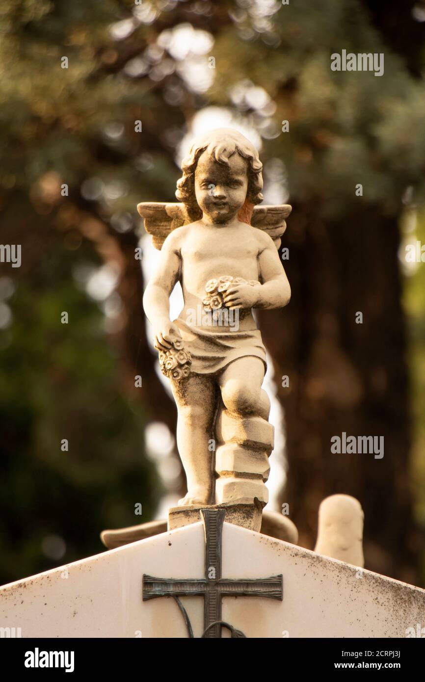 Small statue of a little angel boy with the wings  at the gravestone at the old cemetery in Dalmatia, Croatia, close up on sunlight Stock Photo