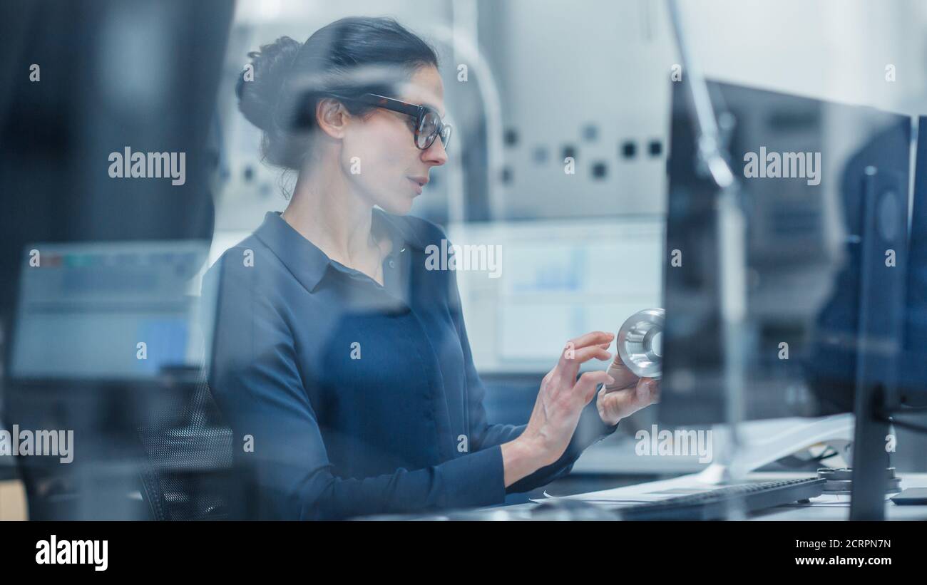 Shot Through Glass. Female Engineer Working on Personal Computer, Inspecting Model of Industrial Machinery Mechanism. She Works in Office that's Stock Photo