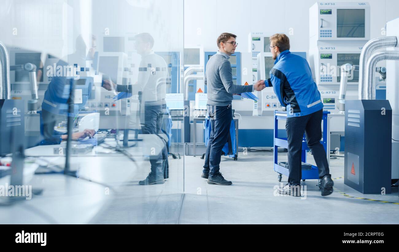 Inside Modern Factory in Facility Workshop Professional Workers Using High-Tech Industrial CNC Machinery, Robot Arm. Professional Industrial Engineer Stock Photo