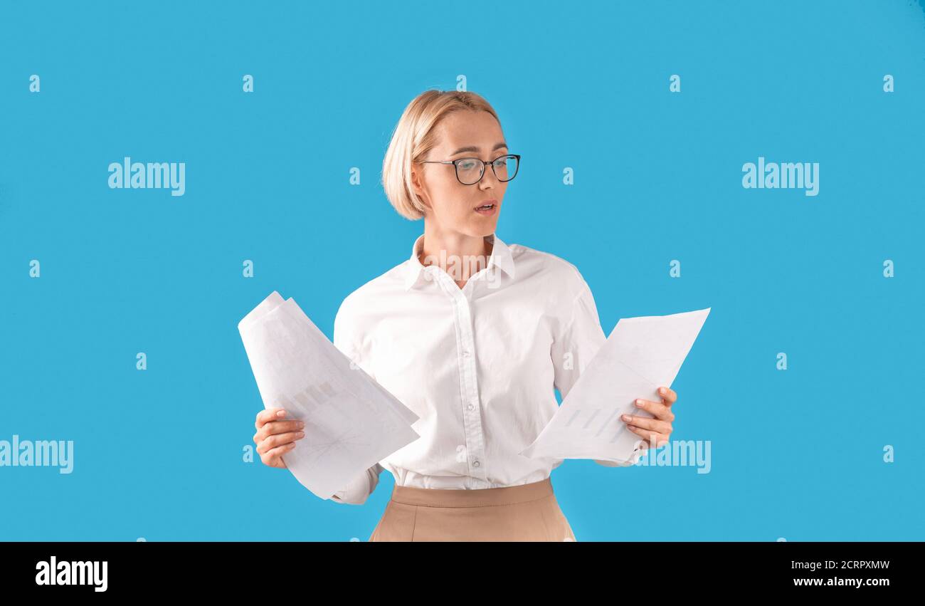 Portrait of serious businesswoman in formal clothes and eyeglasses holding documents over blue studio background Stock Photo