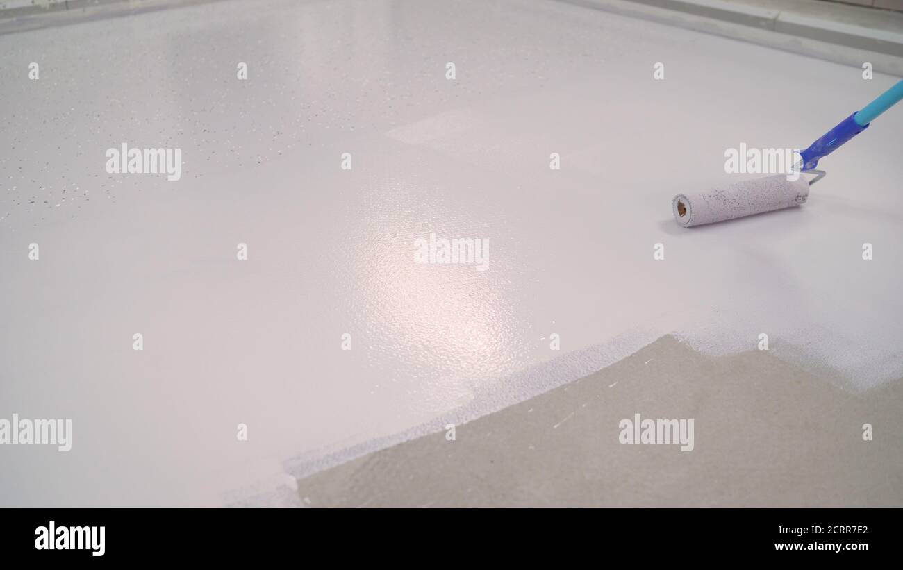 A worker paints the concrete floor with a roller white. Concrete Floor