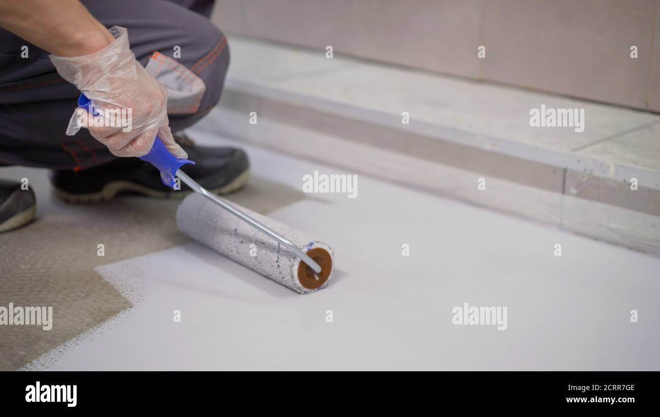 A worker paints the concrete floor with a roller white. Concrete Floor