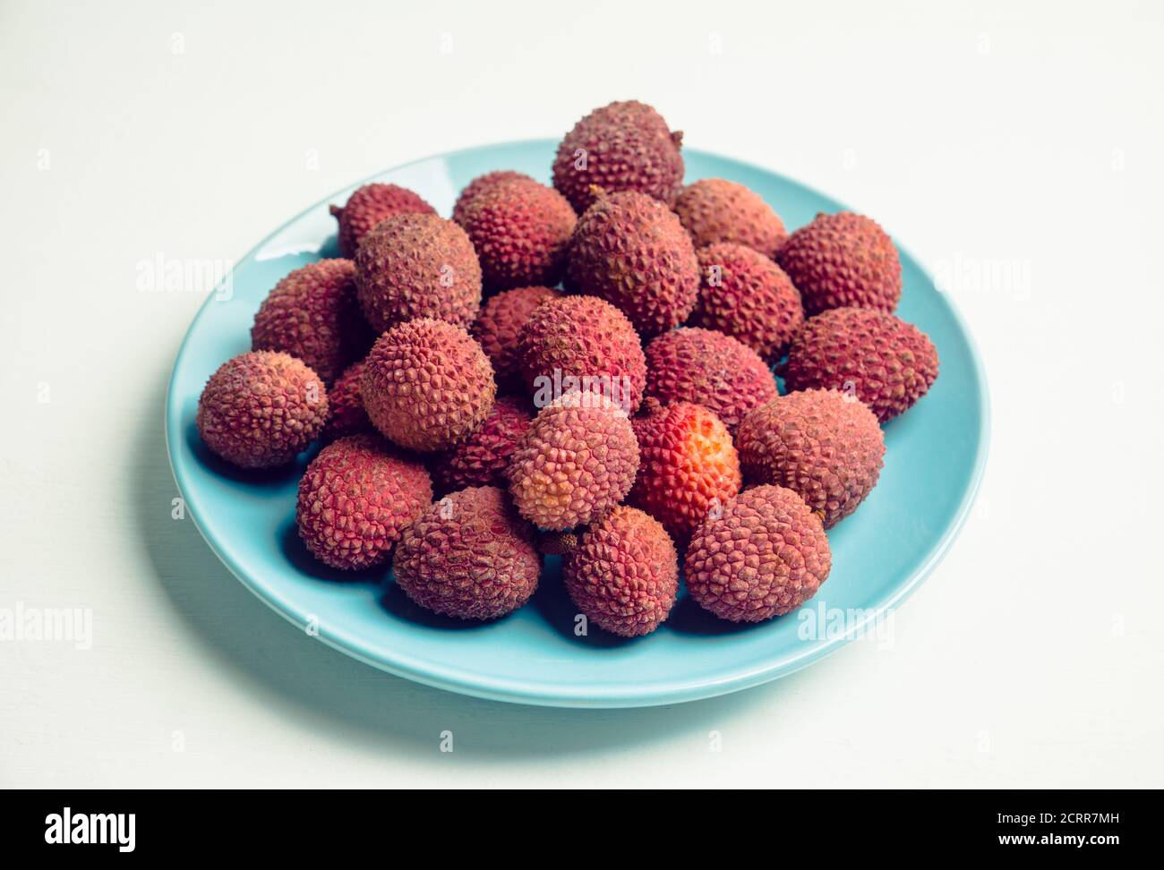 Ripe lychees on the blue plate on white wooden background. Selective focus. Stock Photo
