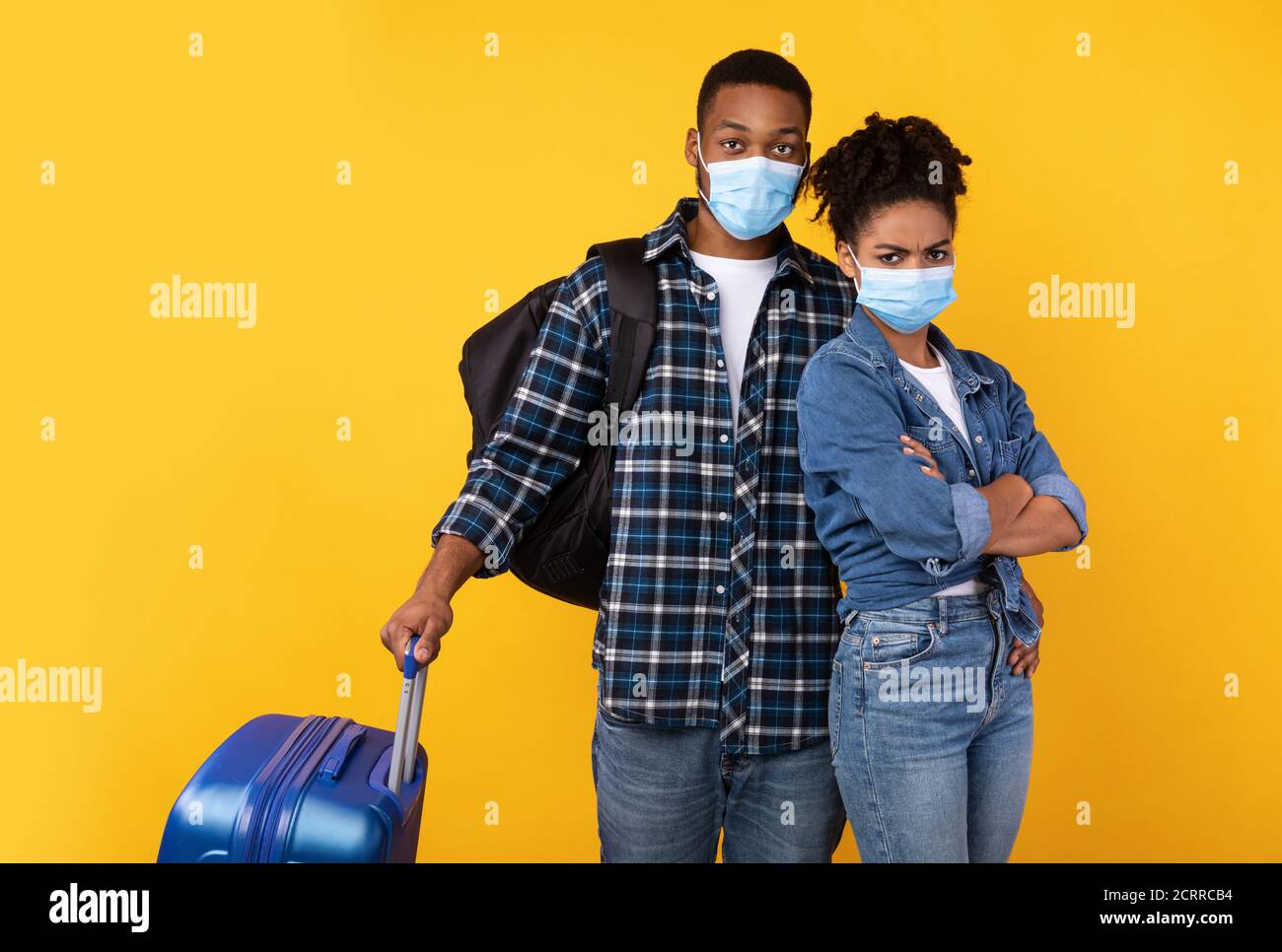 Black Tourists Wearing Medical Masks Standing With Luggage, Yellow Background Stock Photo
