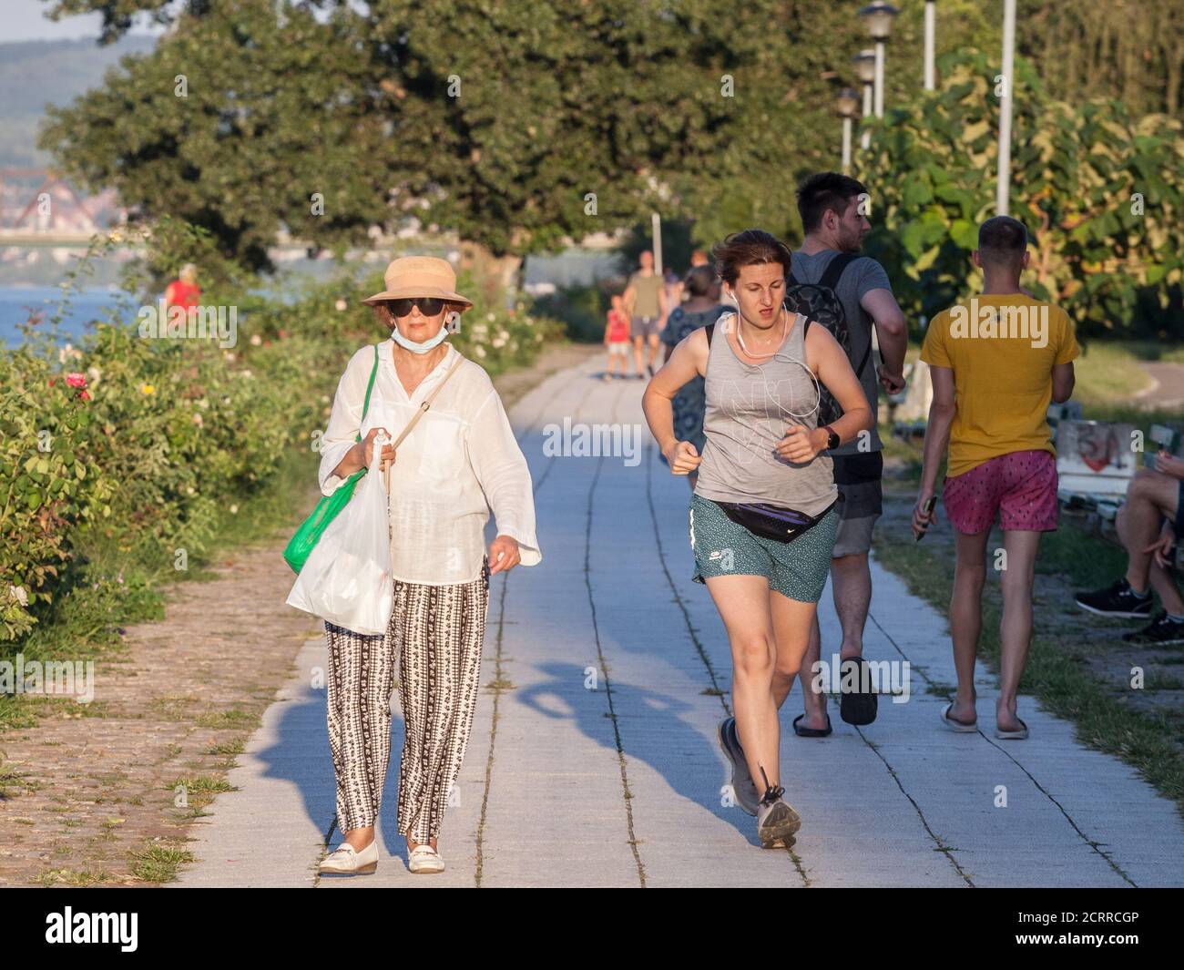 BELGRADE, SERBIA - AUGUST 29 2020: Old woman wwalking with a facemask while a younger girl works out runs next to her without face mask protective equ Stock Photo