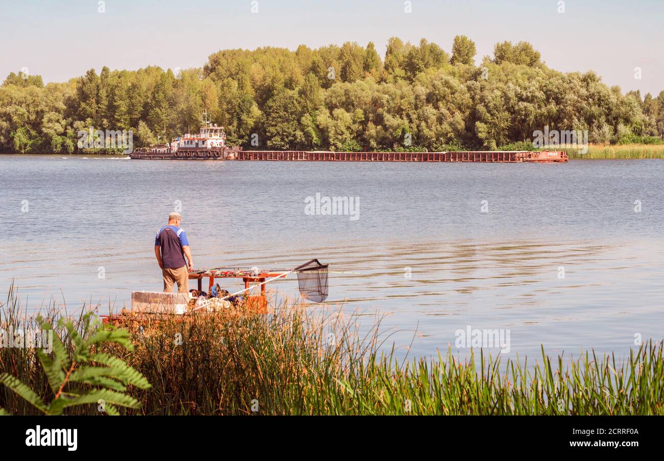 Kiev / Ukraine - September 10, 2020 - A fisherman on the Dnieper River in Kiev, Ukraine during a nice sunny afternoon of summer, is looking a red Barg Stock Photo