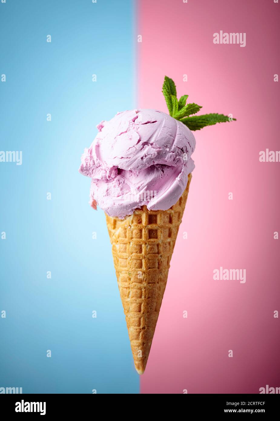 Blueberry ice cream with mint in waffle cone on a blue and pink ...
