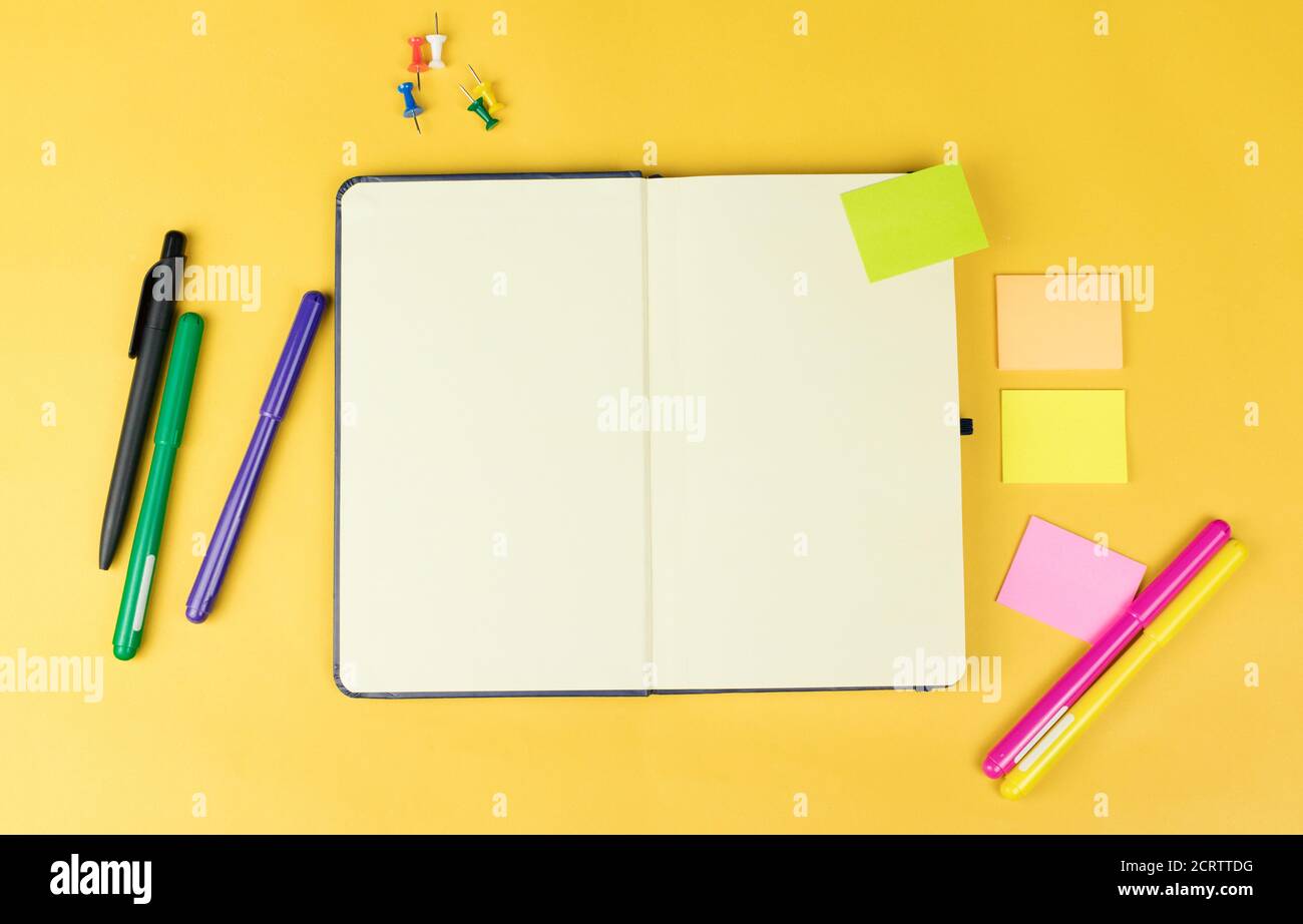 Top view of blank notebook and school supplies like colored markers, sticker and clipers on yellow background, space for text. Stock Photo