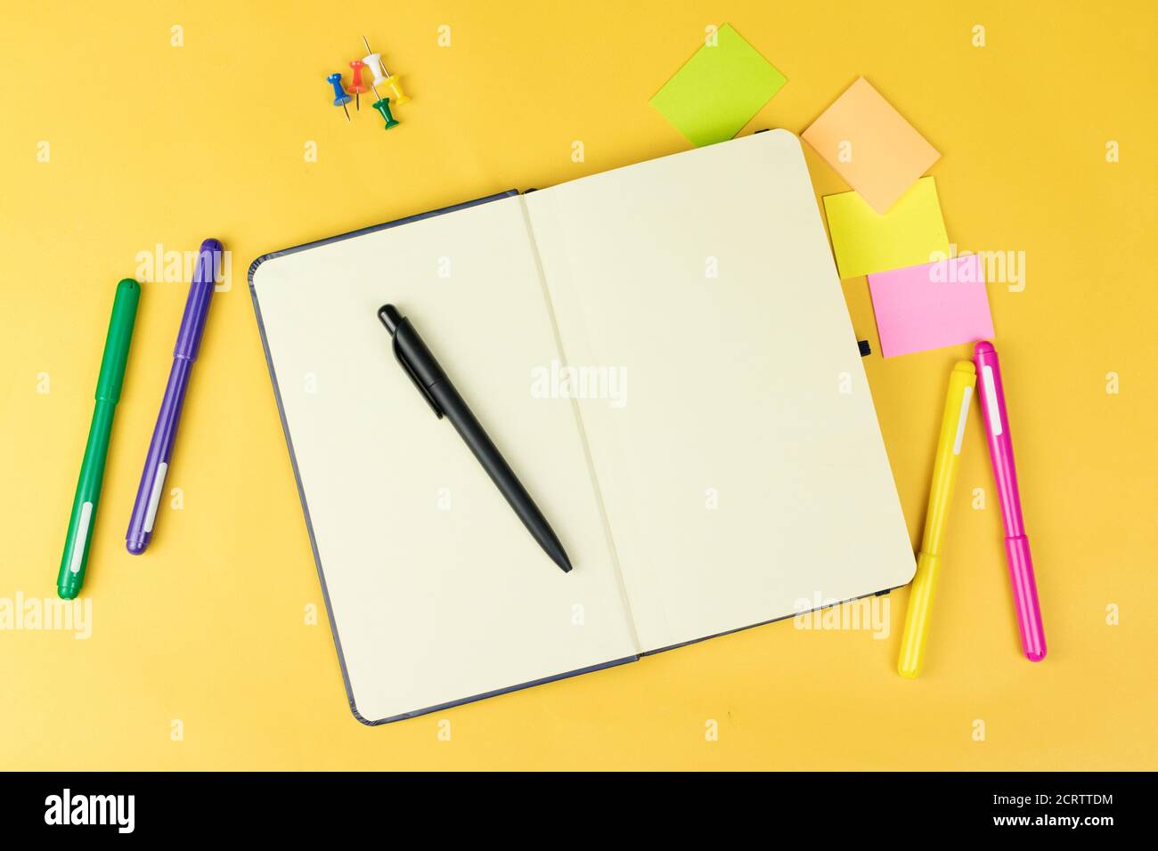 Top view of blank notebook and school supplies like colored markers, sticker and clipers on yellow background, space for text. Stock Photo