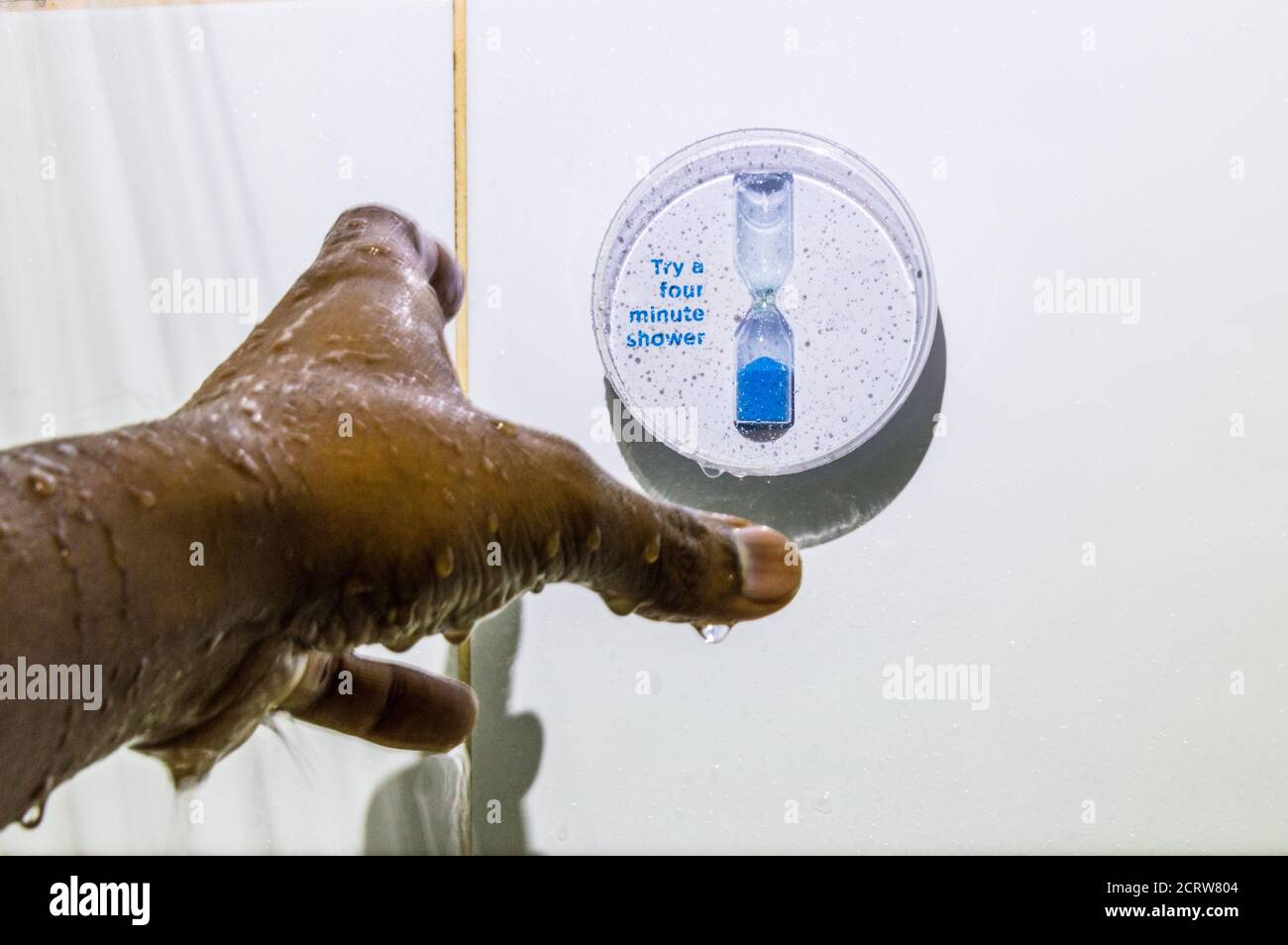 Man wet hand reaching to turn shower timer Stock Photo