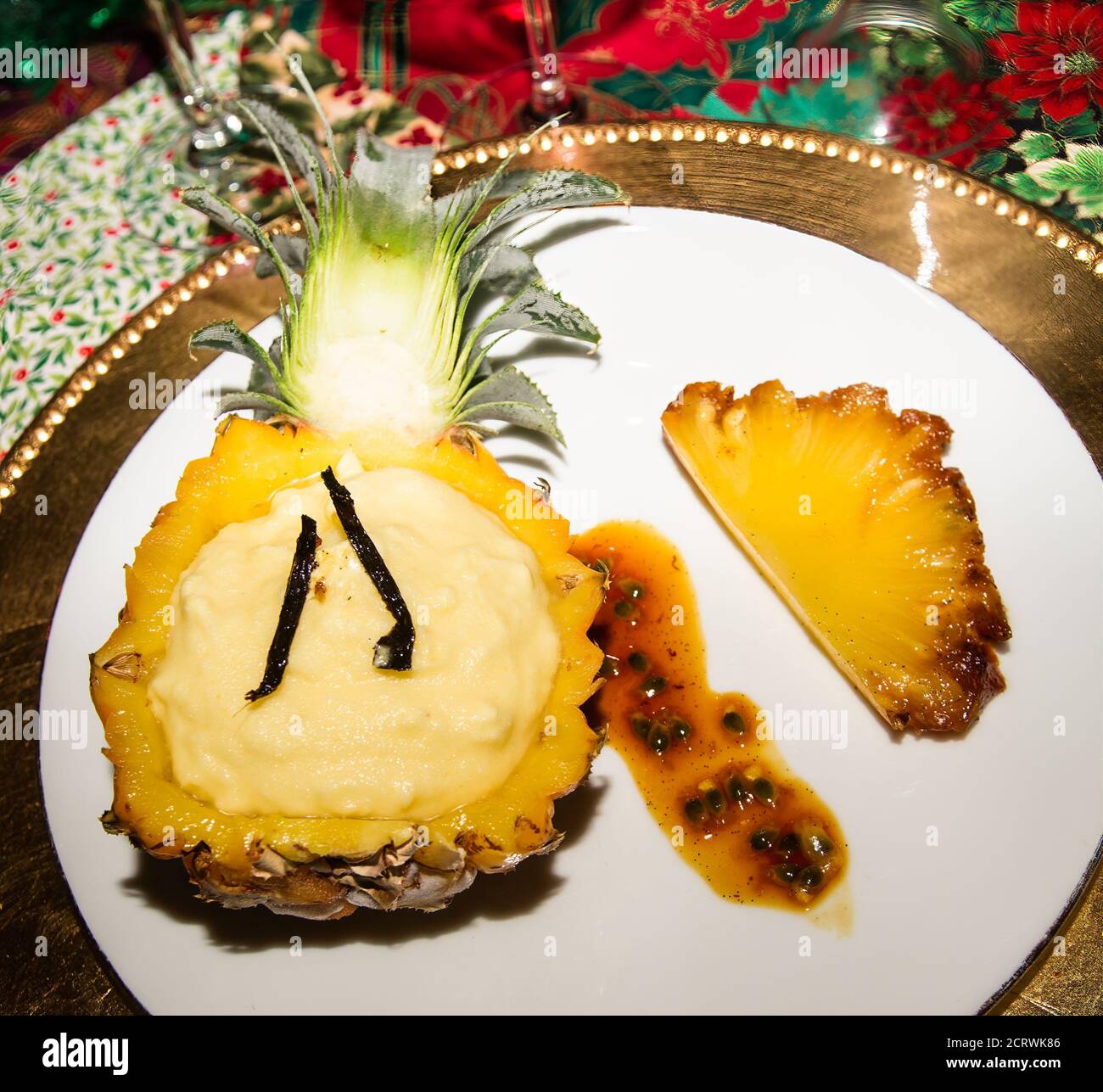 Ice cream and two vanilla pods presented in half a pineapple. And a slice of roasted and caramelized pineapple. Placed on a white and a golden plate. Stock Photo