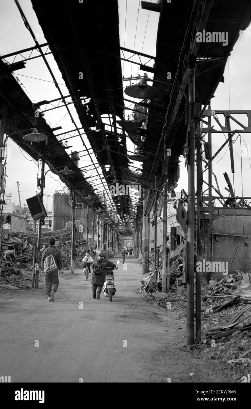 People walking in the burnt downtown ruins in the aftermath of the damage caused by the 1995 Great Hanshin Earthquake in Kobe, Japan. A man can be seen in the distance stopped and praying. Stock Photo