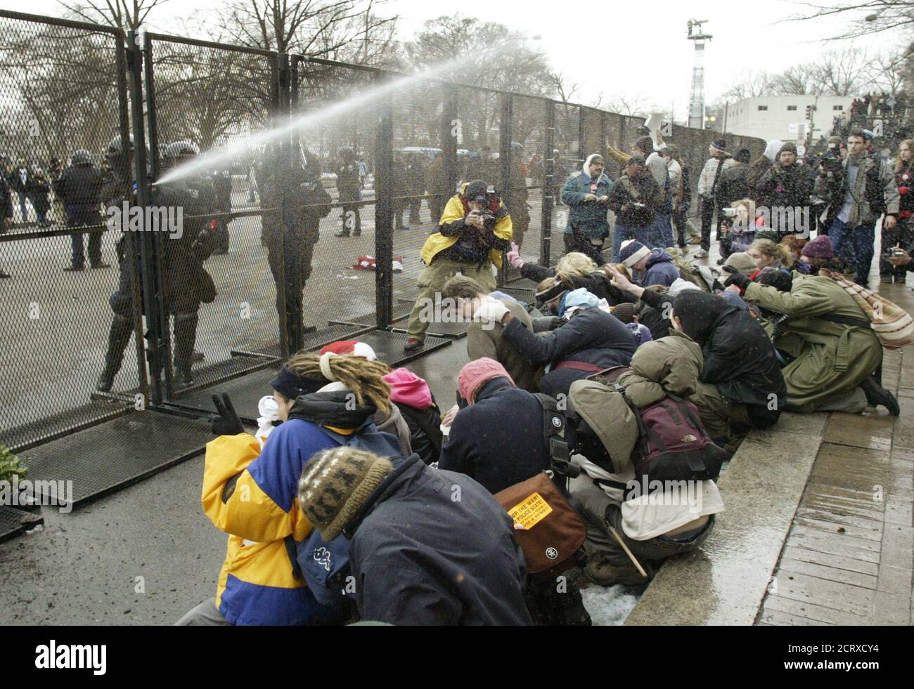 Police officers fire streams of pepper spray over a crowd of protesters after demonstrators threw objects over the fence at police as the Bush inaugural parade passed by on Pennsylvania Avenue in Washington, January 20, 2005. Anti-war chants competed with pomp and circumstance as the inauguration of President George W. Bush for a second term took place amid the barricaded streets of central Washington. REUTERS/Jim Bourg  JRB Stock Photo