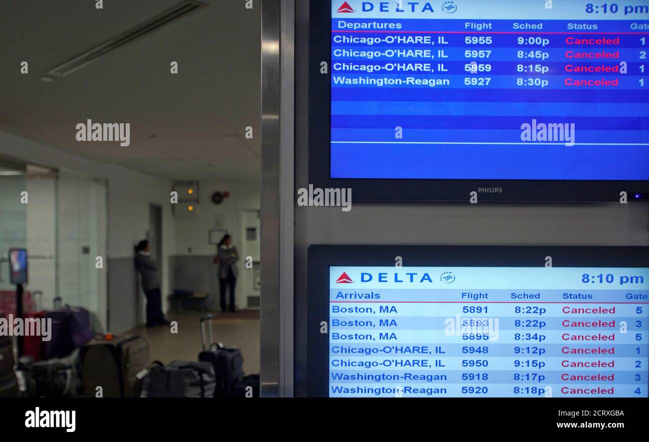 Baggage handlers are seen standing behind a screen that displays information on cancelled flights, after a Southwest Airlines Boeing 737 made an emergency landing at LaGuardia airport in New York July 22, 2013. Several people were injured when the Southwest Airlines Flight 345 with 150 people on board landed at LaGuardia Airport without its nose gear, officials said.   REUTERS/Carlo Allegri  (UNITED STATES - Tags: BUSINESS TRANSPORT DISASTER) Stock Photo