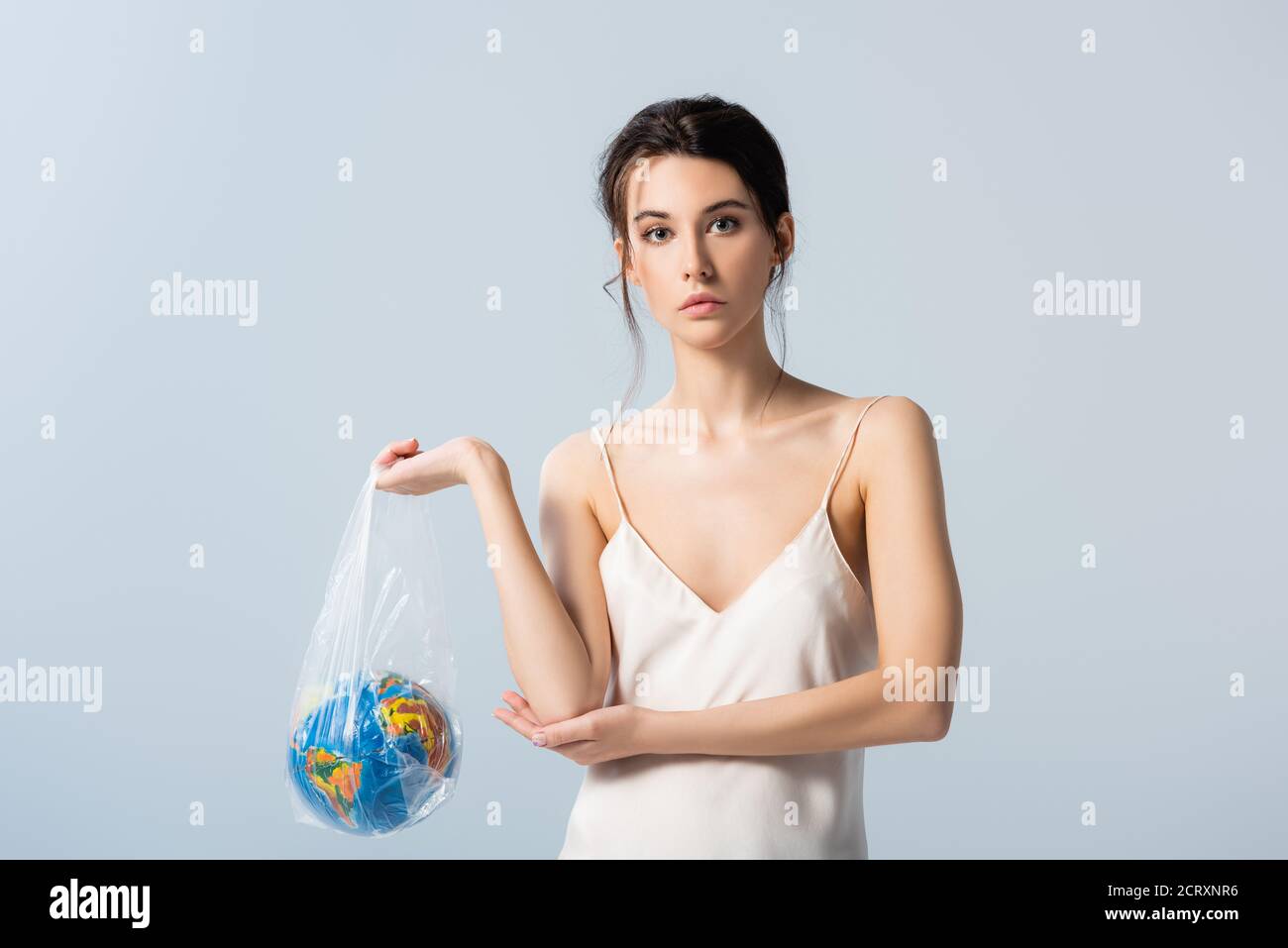 young woman in silk dress holding plastic bag with globe isolated on grey, ecology concept Stock Photo