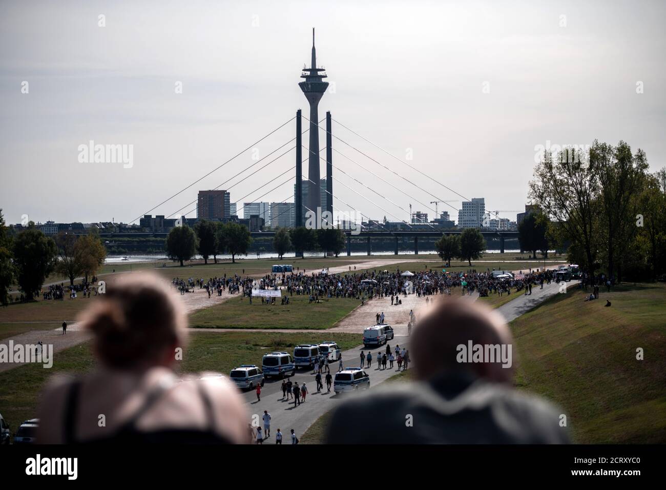 Duesseldorf, Germany. 20th Sep, 2020. People (in front) look from a bridge at police vehicles and participants in a demonstration against the measures to combat coronavirus, who are standing on the meadows of the Rhine. Credit: Fabian Strauch/dpa/Alamy Live News Stock Photo