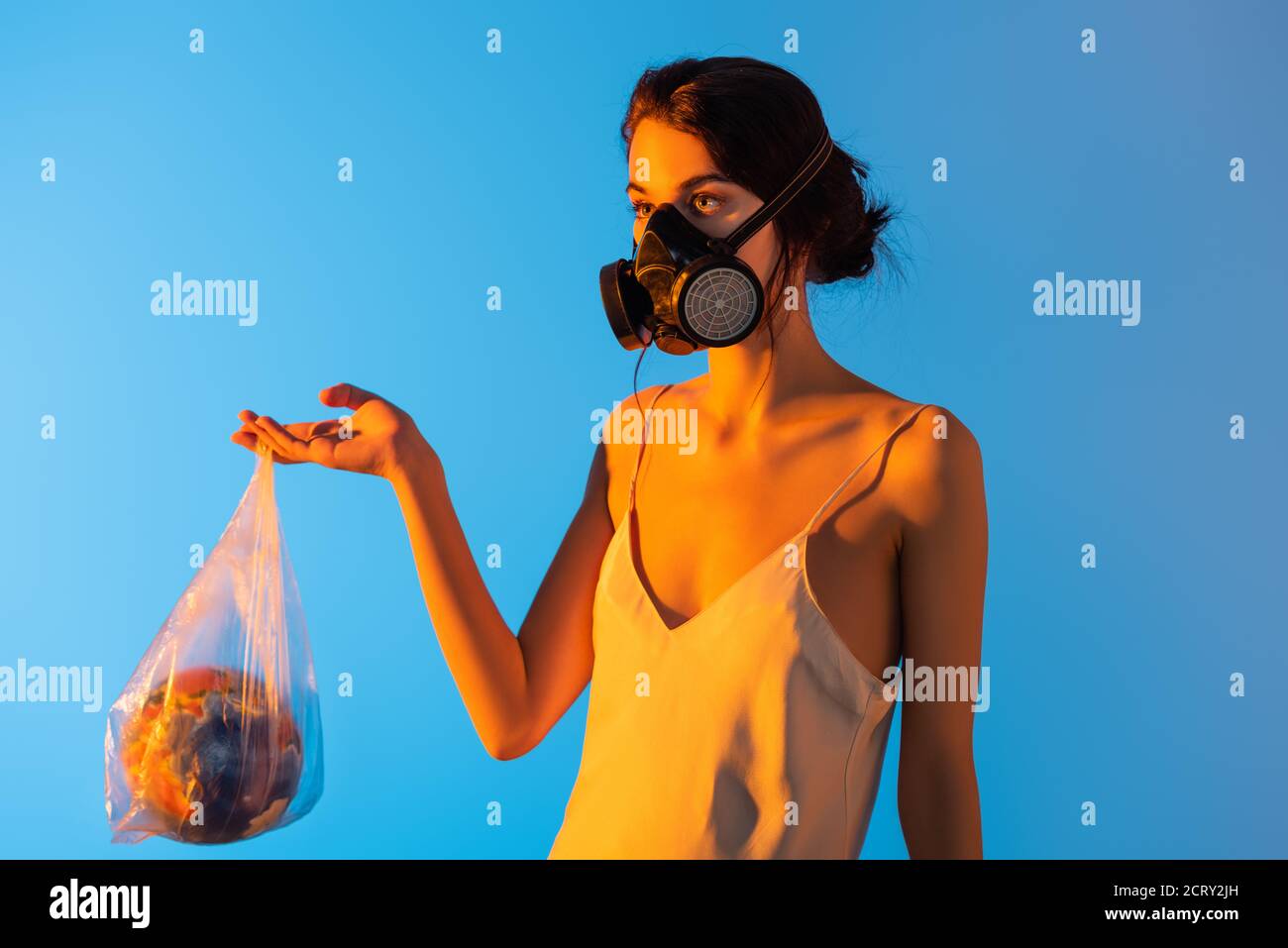woman in gas mask holding plastic bag with globe on blue, ecology concept Stock Photo