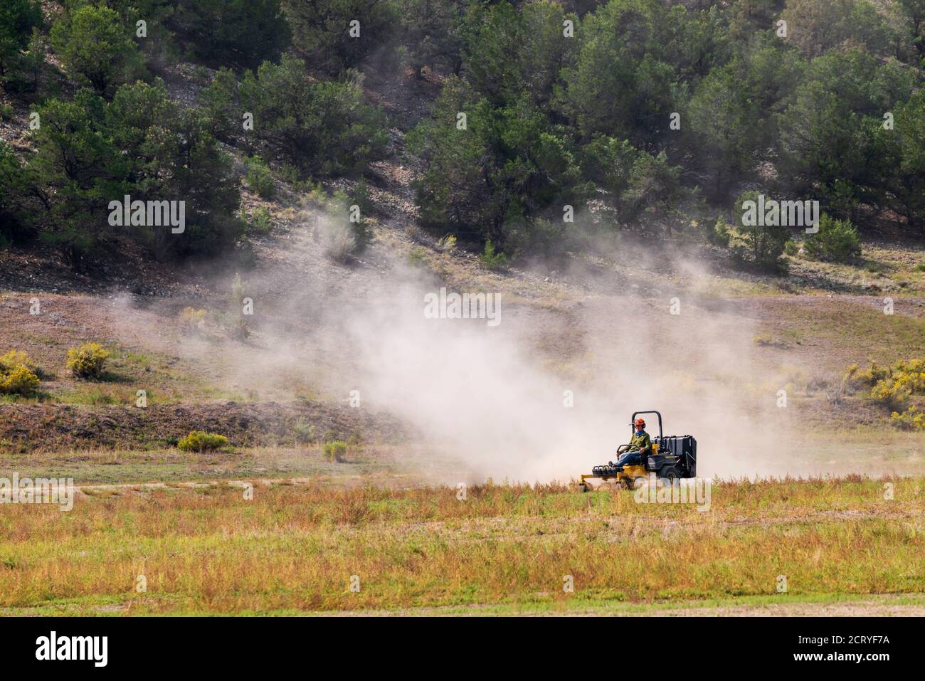 Man mowing dry & dusty pasture with tractor; Central Colorado; USA Stock Photo
