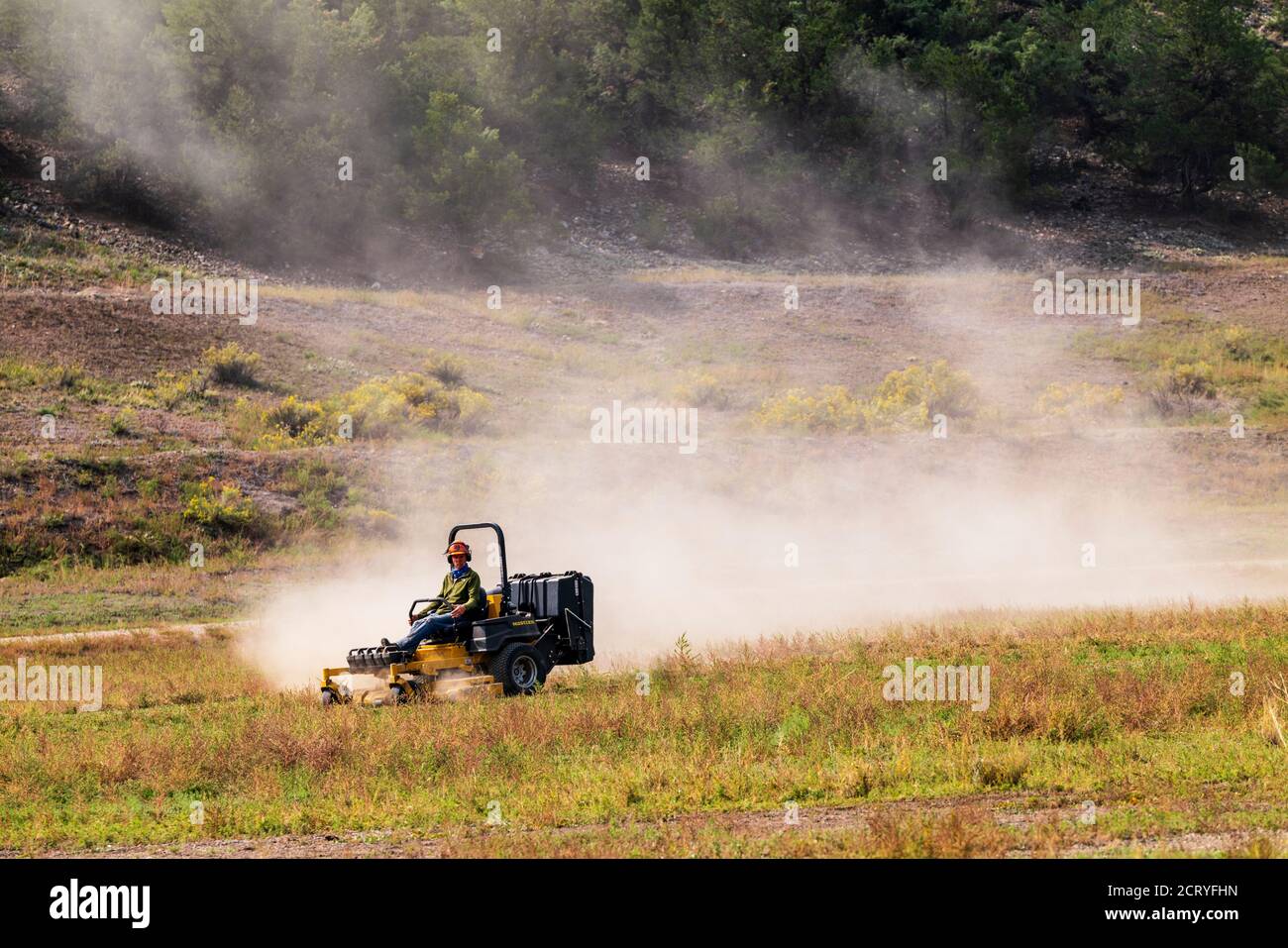 Man mowing dry & dusty pasture with tractor; Central Colorado; USA Stock Photo