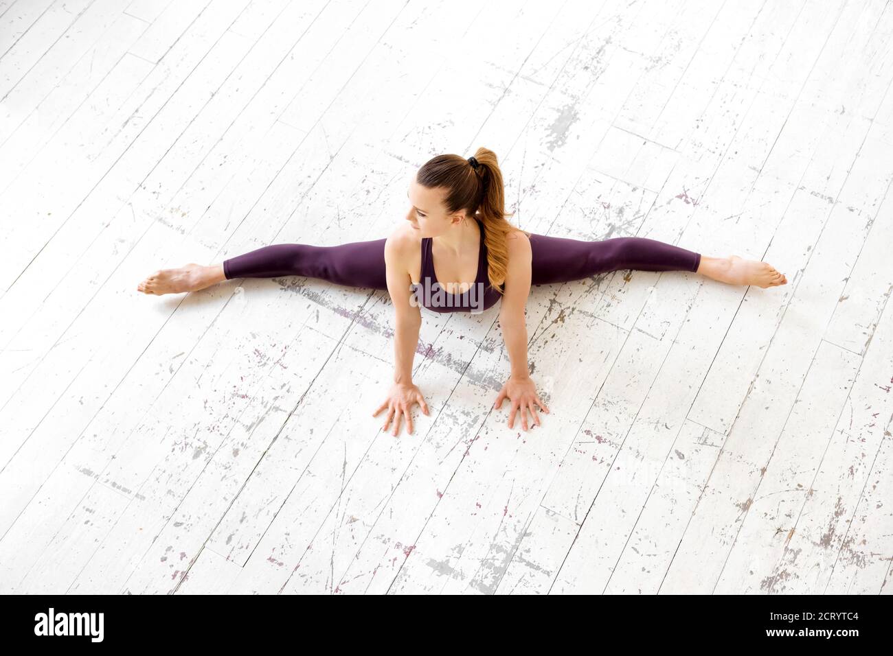 Young female gymnast doing a frontal split pose in a top down view on a white floor in a high key gym in a health and fitness concept with copyspace Stock Photo