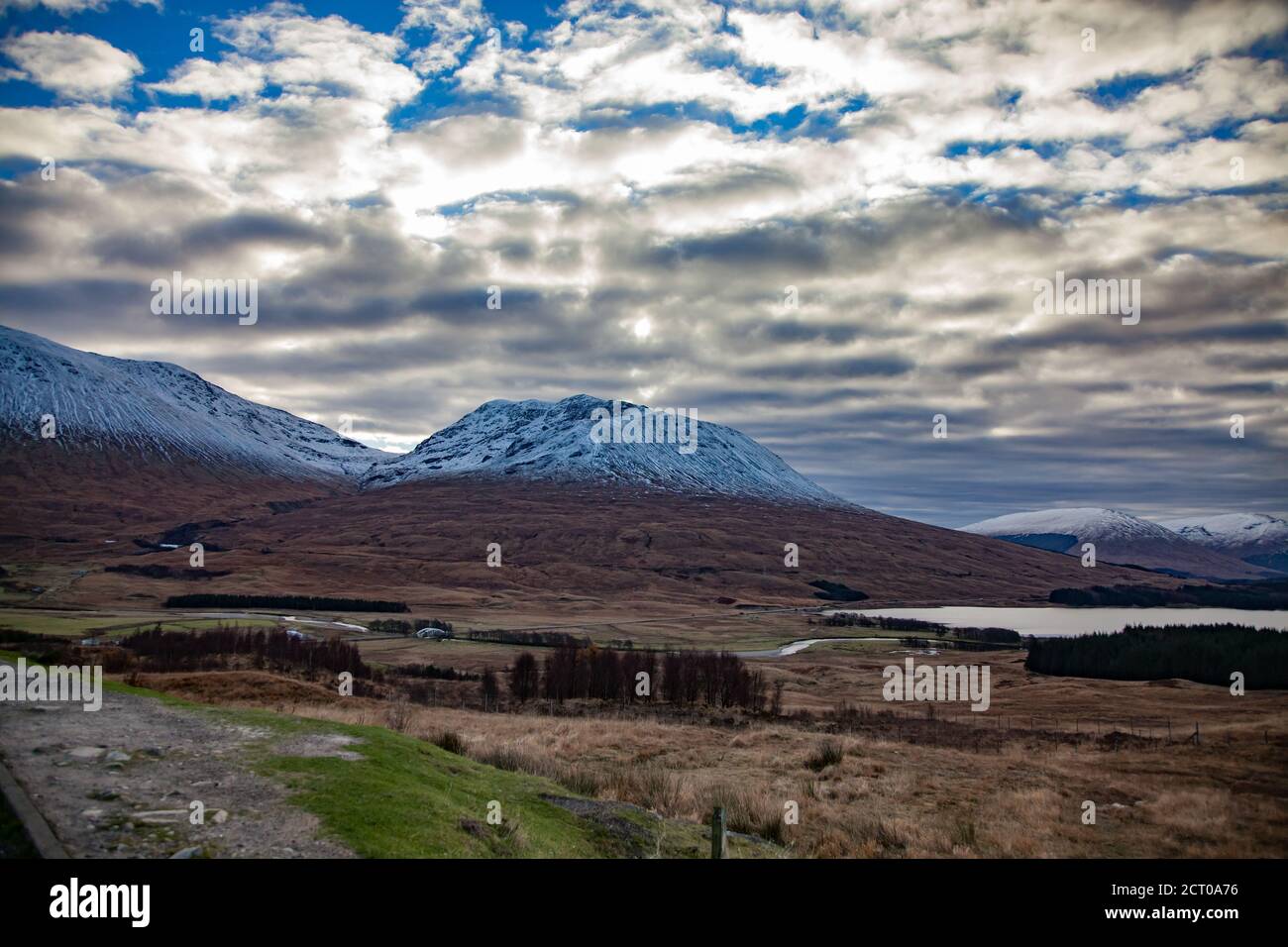 Scottish Highlands in fall. Rural view with river, lake, forest, house and mountains. Peaks with snow. Blue sky with clouds. Stock Photo