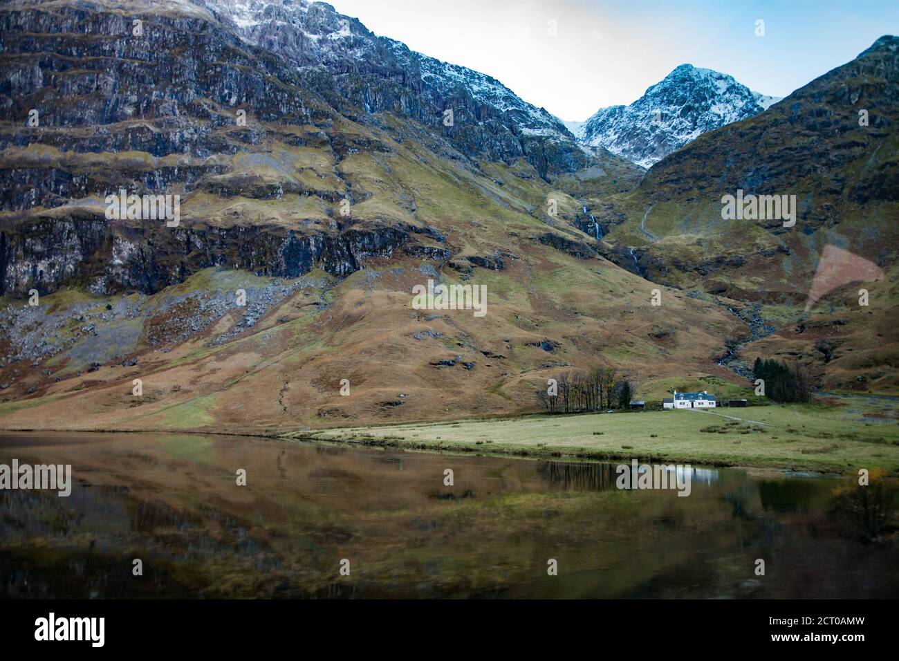 Highlands, Scotland in fall. Rural views with lake, small white house on the beach and mountains. Mountain peaks with snow. Blue sky. Stock Photo