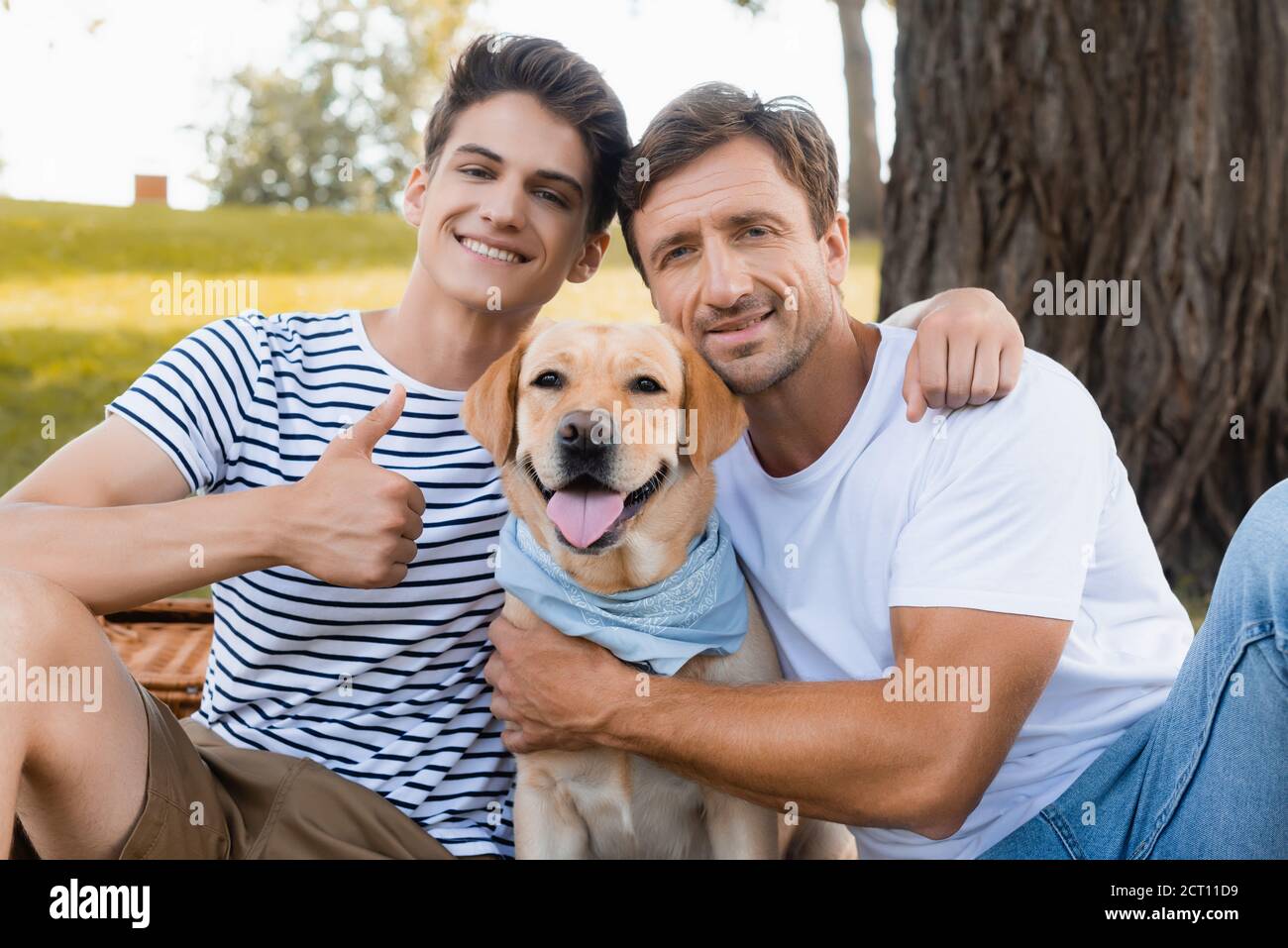 teenager son showing thumb up and hugging father near golden retriever Stock Photo