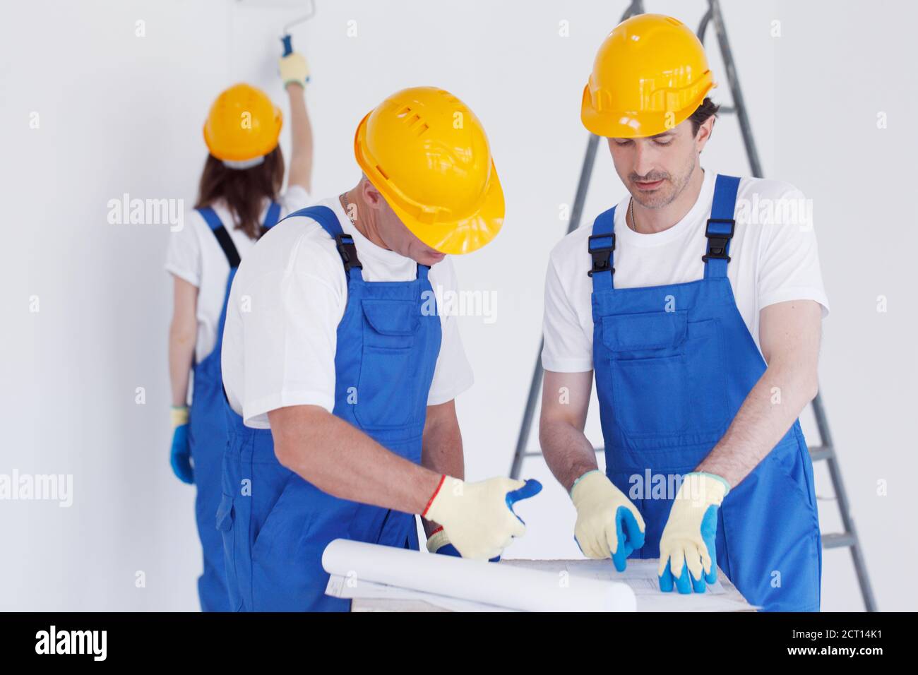 Building, renovation, repair, teamwork and people concept - close up of builders discussing blueprint indoors woman painting wall on backround Stock Photo