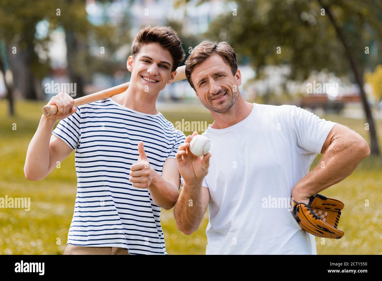 teenager boy with softball bat showing thumb up near father in leather